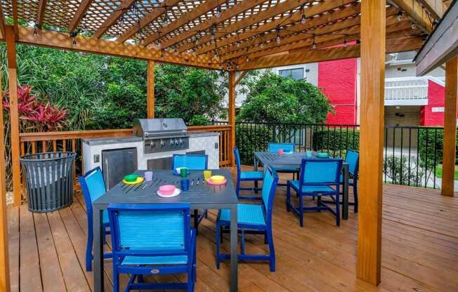 Fusion Orlando apartments outdoor grilling area with tables and chairs, grill and prep counters, and trash can under stained wood trellis.