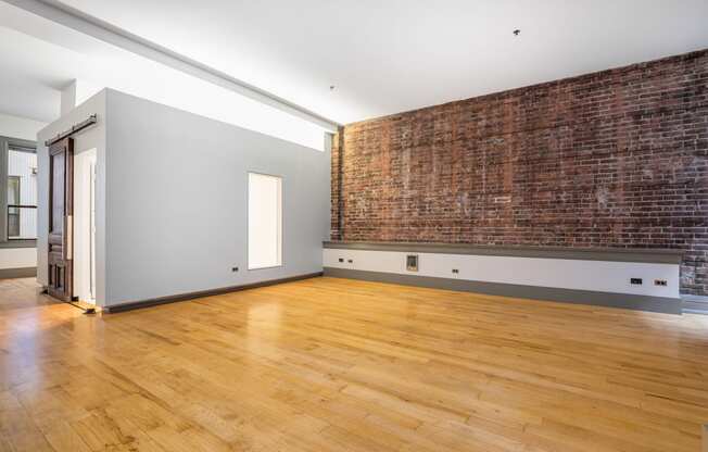 an empty living room with a brick wall and wooden floors