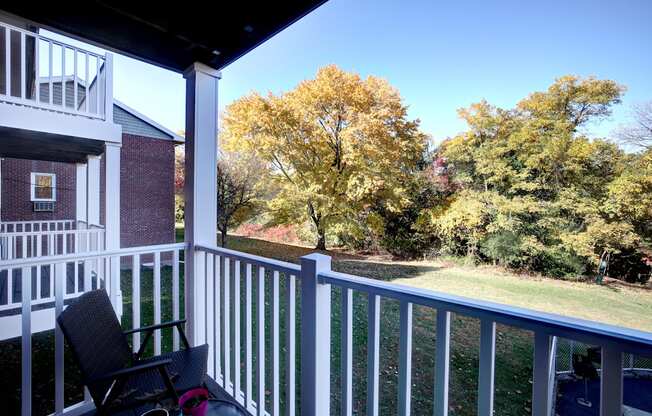A chair is on a porch with a view of trees.