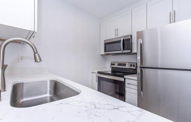 Modern kitchen interior featuring a stainless steel refrigerator, microwave, and stove. The countertop is made of white marble, and there is a sleek, modern sink. The cabinets are white with clean lines, creating a bright and contemporary atmosphere.