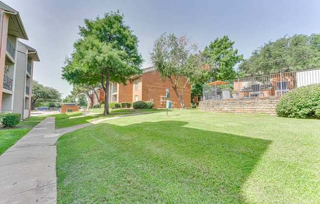 A grassy area with a sidewalk and a building in the background at Copper Hill Apartments, Bedford, Texas
