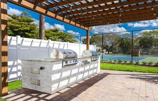 A white outdoor kitchen with a grill and a pergola.