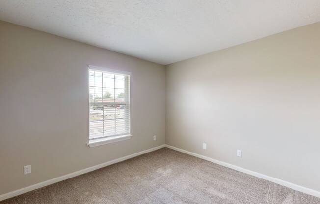an empty bedroom with a window in the corner