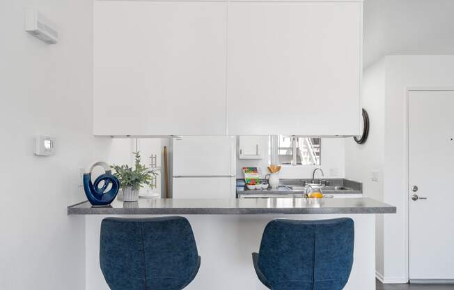 a kitchen with white cabinets and a counter with two blue chairs