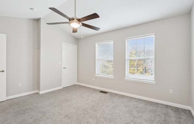 A room with a ceiling fan and two windows.