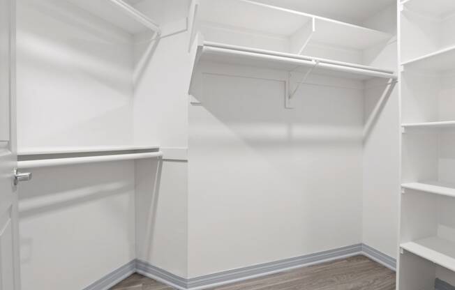 a walk in closet with white walls and wood flooring