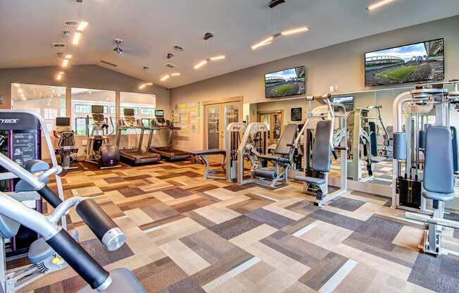 a spacious fitness center with cardio equipment and flat screen tvs