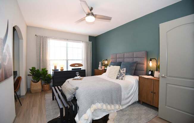 A bedroom with a bed, a chair, a ceiling fan, and a window.