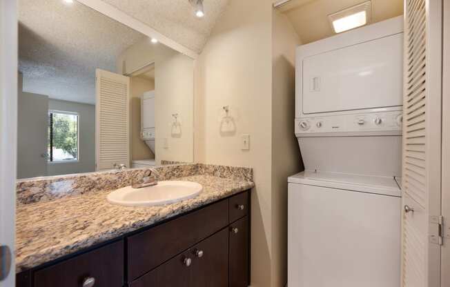 Bathroom with large mirror, granite vanity with sink and larger sized washer and dryer nearby.