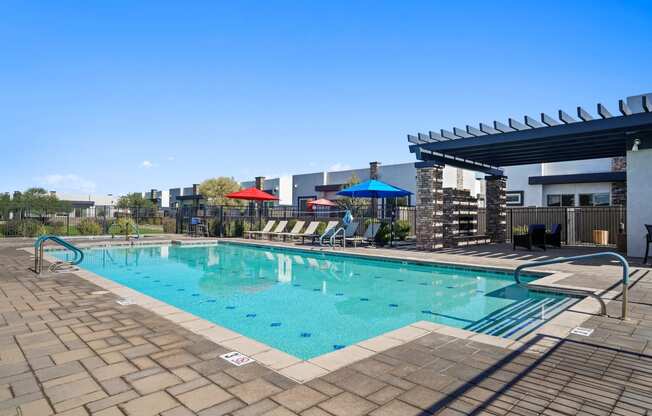 a resort style pool with lounge chairs and umbrellas next to a building