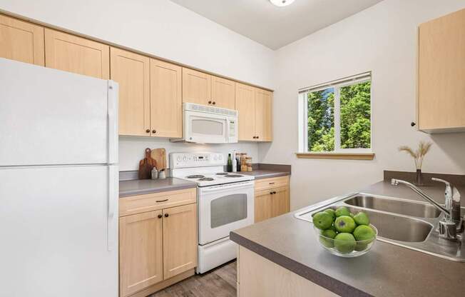 Jackson floor plan kitchen with a white refrigerator, wooden cabinets, and microwave at The Madison apartments in Olympia, WA