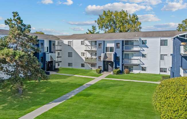 an exterior view of an apartment building with a lawn and sidewalk