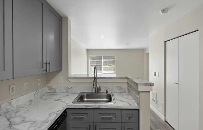 Cozy Kitchen with a Sink, Plank Flooring, and a View Into the Living Room with a Window at Excalibur Apartment Homes, Bellevue