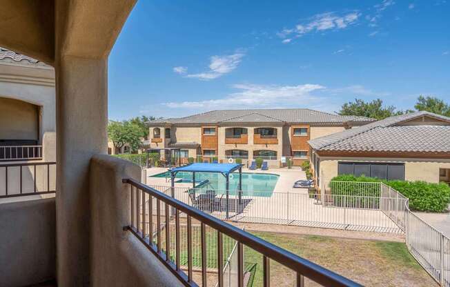 A view from a balcony looking out at a pool and a building.