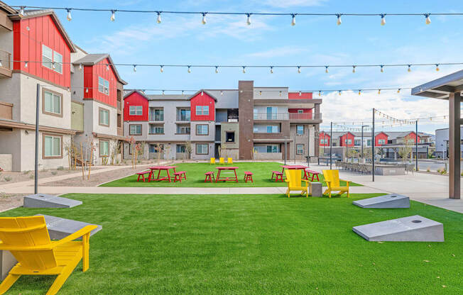 A grassy area with picnic tables and benches in front of apartment buildings.