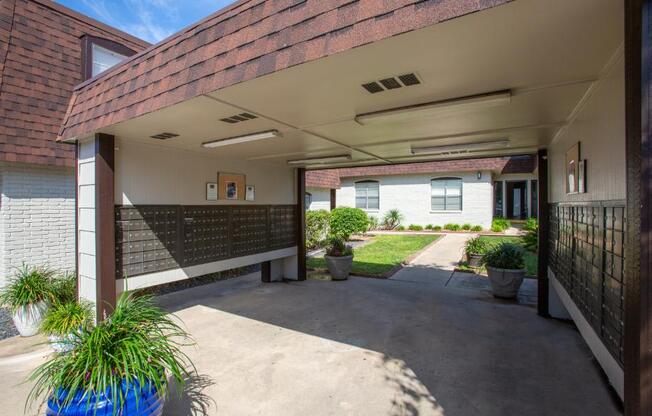 A covered walkway leads to a white building with a brick wall and a black fence.