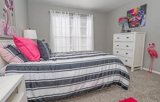 Model bedroom with a bed, nightstand, and a pink flamingo decoration at Maplewood apartments in Shreveport, LA.