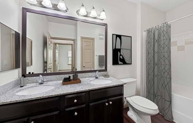 A bathroom with a large mirror, two sinks, and a toilet.