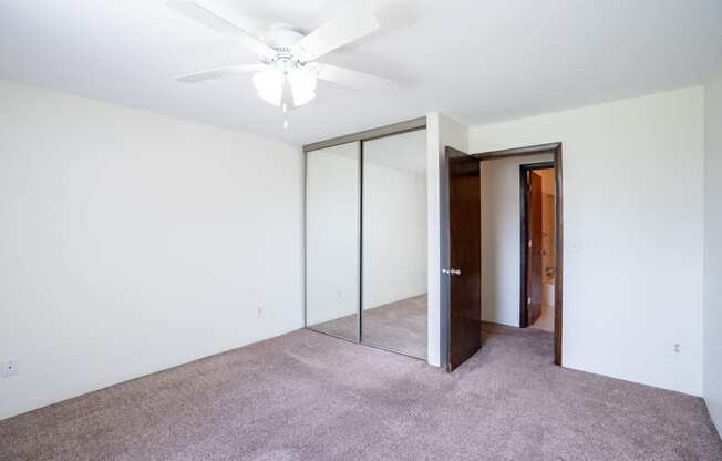 a bedroom with a ceiling fan and mirrored closet. Coon Rapids, MN Robinwood Apartments