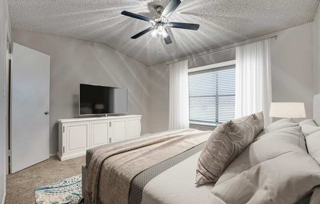 A bedroom with a bed, a television, and a ceiling fan.