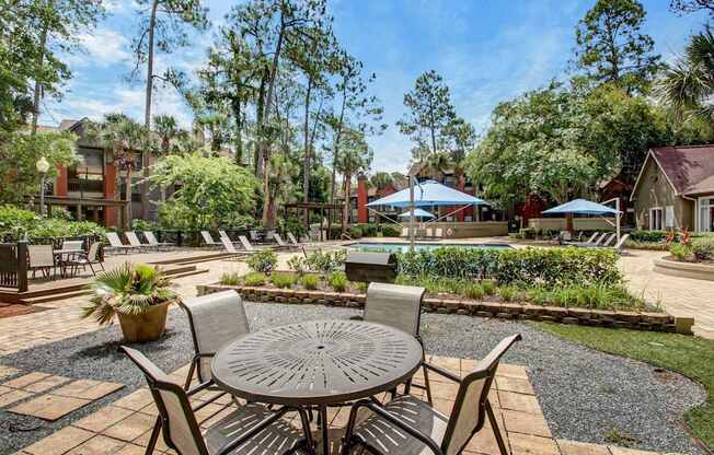A patio with a table and chairs is surrounded by greenery.