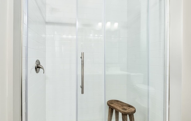 A wooden stool is in front of a glass shower door at The Ashton at East Park Apartments, Georgia, 30144