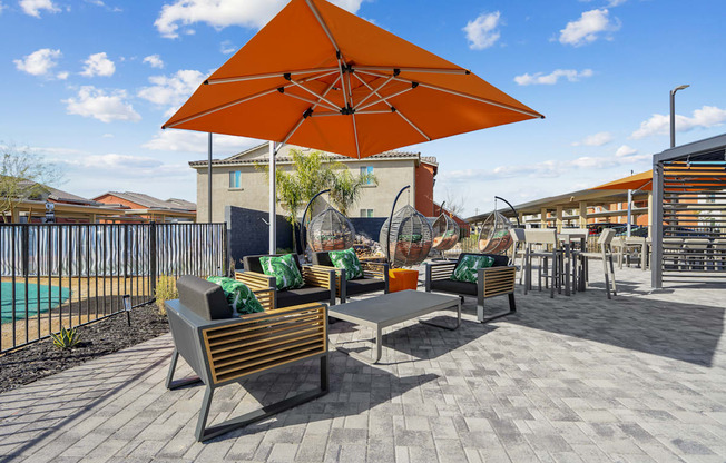 A patio with a table and chairs under an orange umbrella.