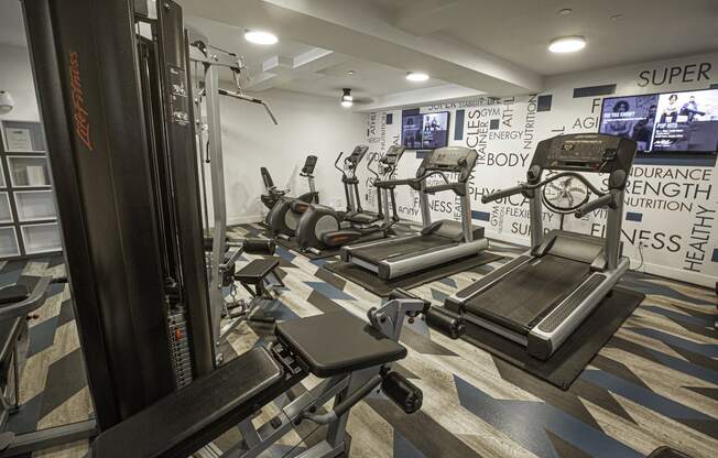 a gym with treadmills and other exercise equipment in a room with TV's on the wall