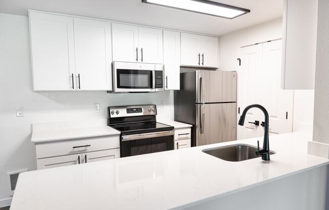 a white kitchen with stainless steel appliances and white counter tops