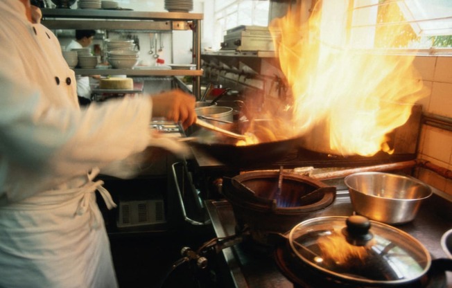 a chef cooking food in a kitchen with a fire