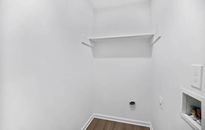A small white room with a shelf and a wood floor.