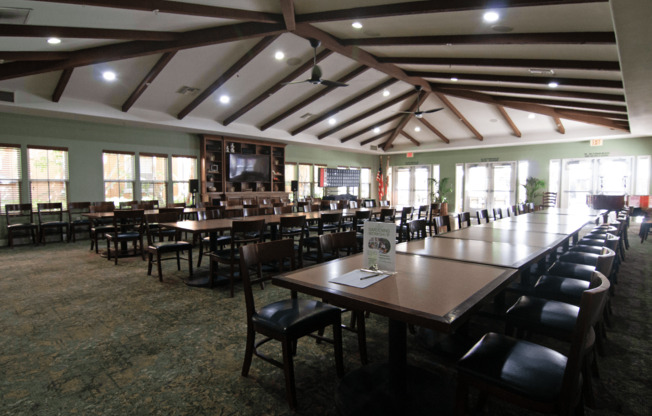 A large room with tables and chairs and a screen tv.,A large room with tables and chairs and a screen tv.
