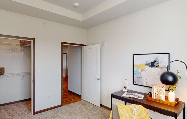 A functional bedroom here at Van Buren East with soft carpeting and neutral walls. A spacious closet and dedicated workspace area create a comfortable, practical, and inviting living environment.