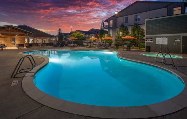 a swimming pool at dusk at a hotel with a sunset in the background