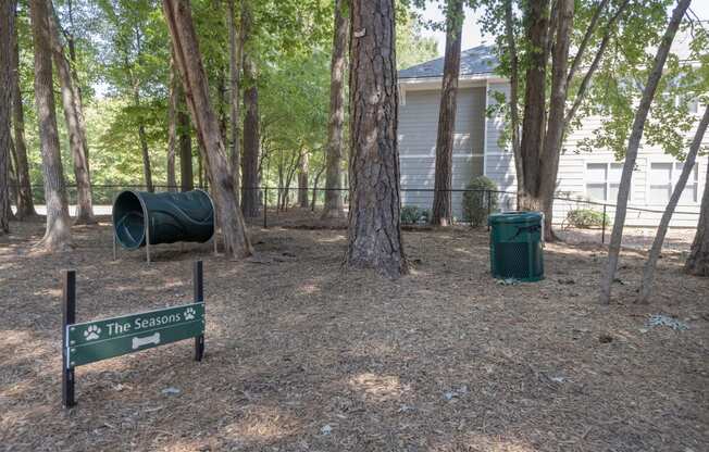 Bark park surrounded by trees with dog exercise equipment at  Seasons at Umstead apartments in Raleigh