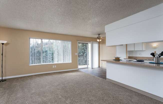 an empty living room with a kitchen and a door to a patio