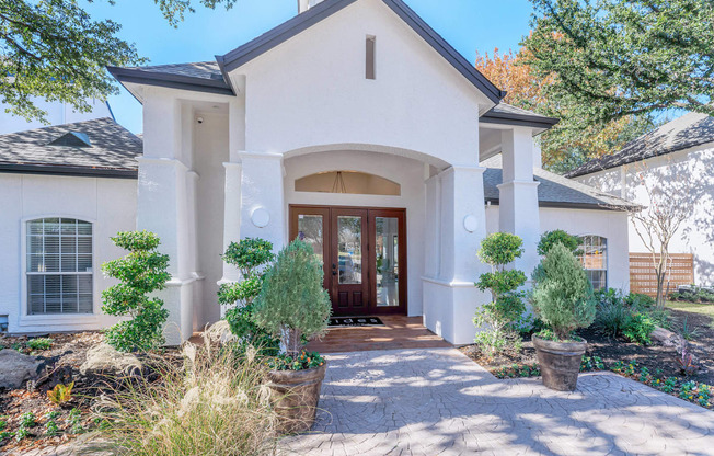 a house with white walls and a front porch with potted trees and shrubs