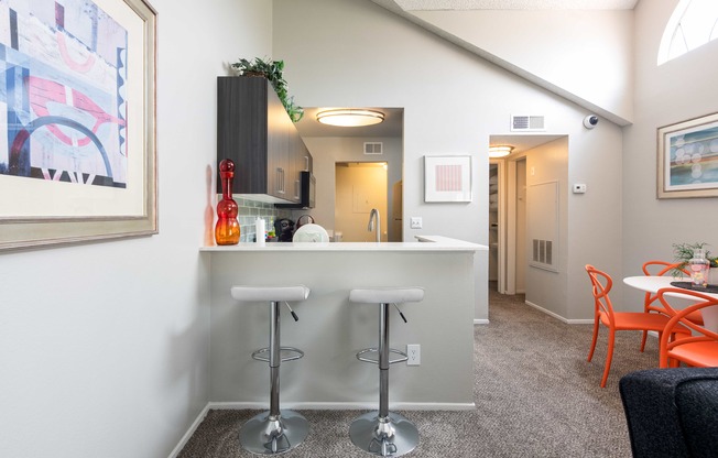 a bar with three stools in a living room with a kitchen and a hallway