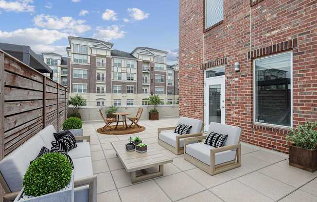 A patio with a white couch, a wooden table, and a brick building in the background.