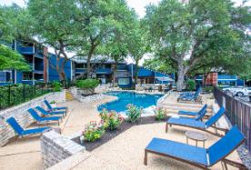 A pool surrounded by trees and lounge chairs.