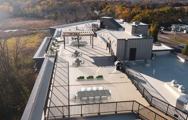 A rooftop patio with a black railing and a few chairs and tables.