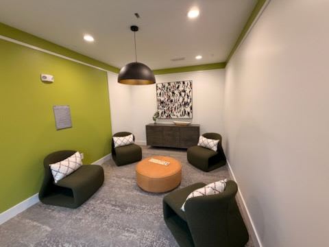 A room with green walls and grey carpet has a large brown ottoman in the middle.