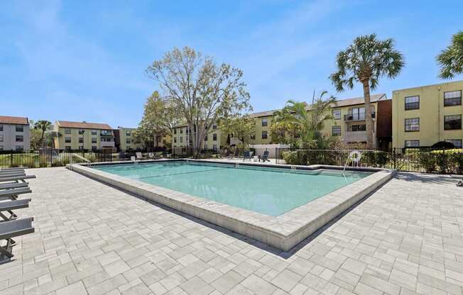 A swimming pool surrounded by a brick patio and palm trees.