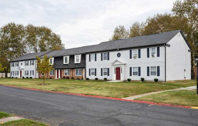 A white building with a red door is situated on a street.