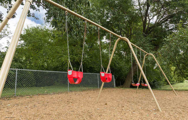A playground with a swing set and two red swings.