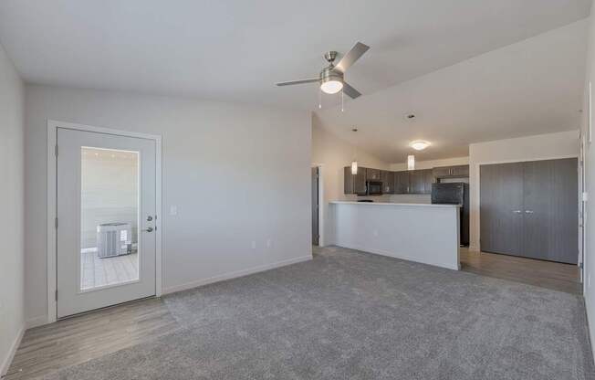 A spacious living room with a grey carpet and a ceiling fan.