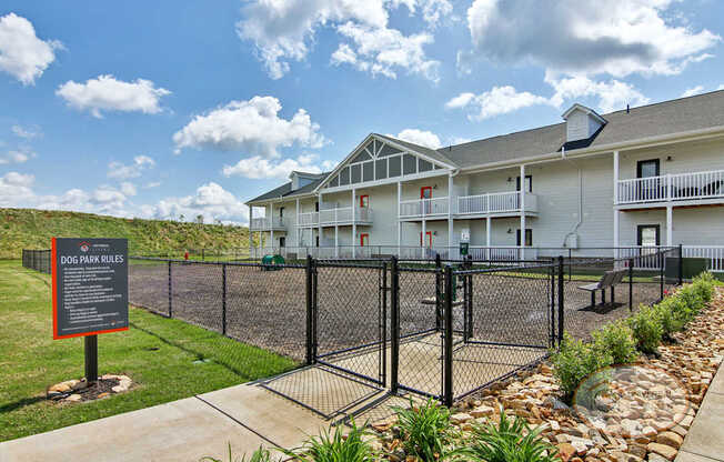 A fenced in dog park with an apartment building in the background.