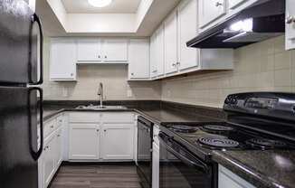 A black refrigerator is in a kitchen with white cabinets.