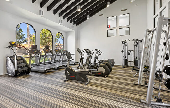 Community Fitness Center with Equipment and Window View at Hilands Apartments in Tucson, AZ.