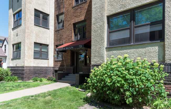 the front of a brick apartment building with a sidewalk and bushes